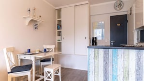 Een kleine keuken met een houten kookeiland, een eethoek met stoelen en een wandplank met decoratieve objecten.