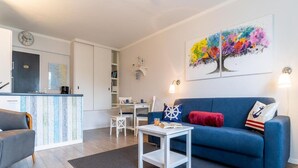 Een moderne woonkamer met een blauwe bank, een witte bijzettafeltje en een kleurrijk abstract schilderij aan de muur.