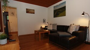 A living room with a wooden floor, a black leather sofa, a wooden coffee table, and a painting on the wall. - Ferienhaus in der Nahe des Sees, Haustierfrei (Clausthal-Zellerfeld)