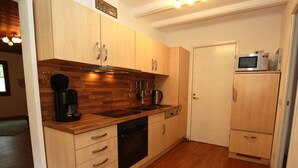 A compact kitchen with wooden cabinets, a built-in oven, a coffee maker, and a microwave on a shelf. - Ferienhaus in der Nahe des Sees, Haustierfrei (Clausthal-Zellerfeld)