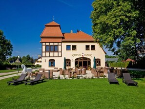 Un bâtiment sur lequel on peut lire l’inscription « CHEVAL BLANC », ainsi qu’une terrasse aménagée avec des chaises longues et une statue de cheval.