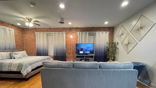 A modern living room with a grey sofa, a TV, and a brick wall.