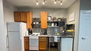 A compact kitchen with wooden cabinets, a white refrigerator, a stove, a microwave, and a sink.