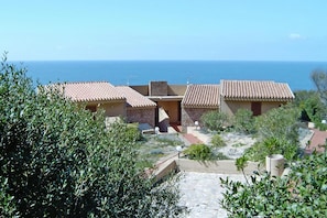 A coastal property with terracotta-roofed buildings, a stone pathway, and a view of the sea. - Holiday Home in Sardinia Near Red Cliffs (Trinità d'Agultu e Vignola)