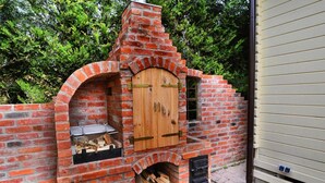 A brick-built outdoor oven with a wooden door, a shelf for grilling, and a fire pit below. - Chalet in Grzybowo Near the Beach (Kołobrzeg)