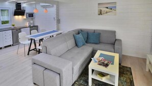 A modern living room with a grey sofa, a small coffee table, and a dining area with a white table and chairs. - Chalet in Grzybowo Near the Beach (Kołobrzeg)