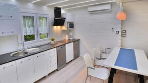 A modern kitchen with white cabinetry, a black range hood, and a dining area with a blue table runner. - Chalet in Grzybowo Near the Beach (Kołobrzeg)