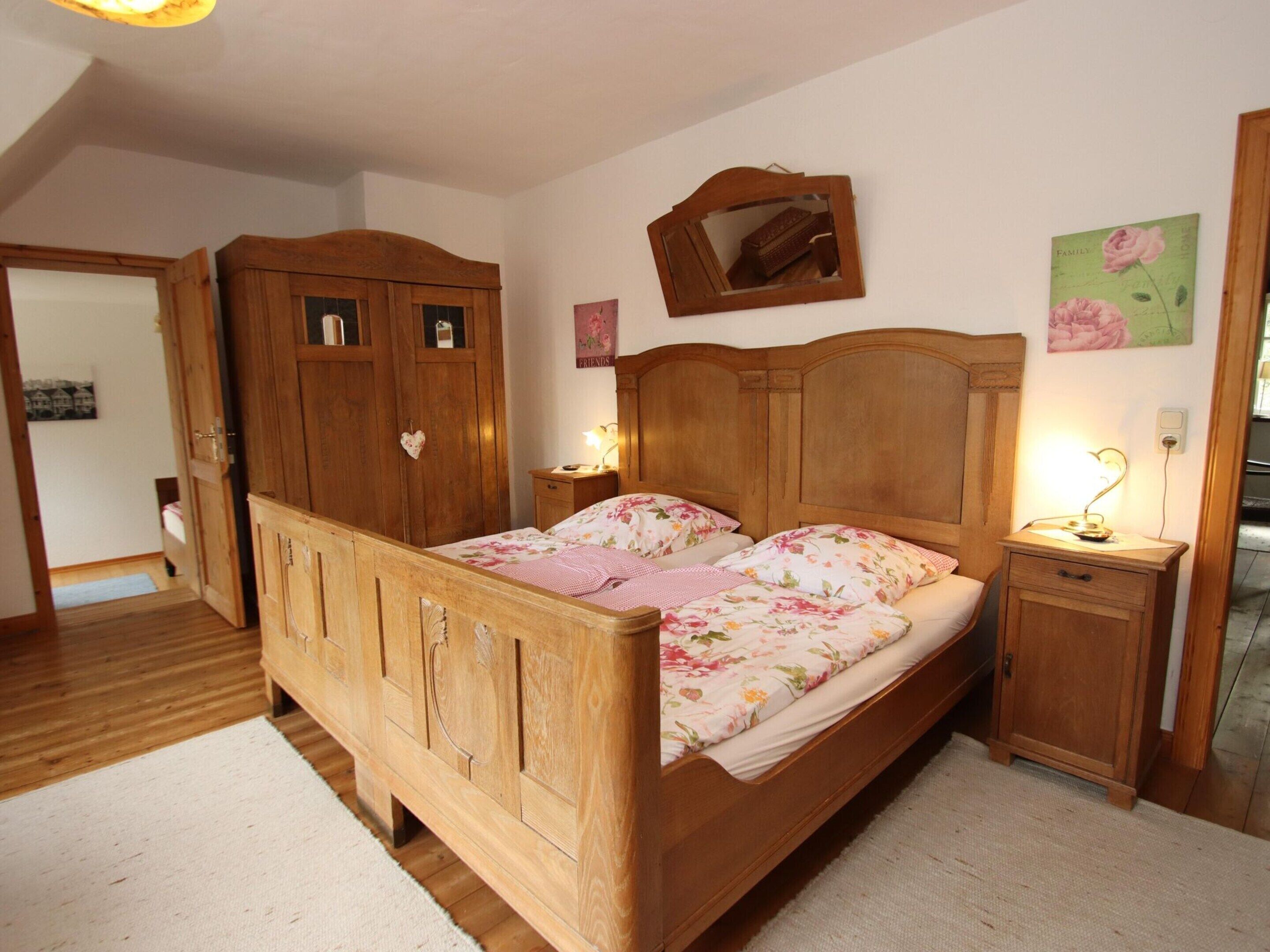 Quarto com cama de madeira, guarda-roupa, mesa de cabeceira com abajur e espelho na parede.