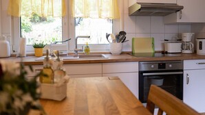 Una cocina con una mesa de madera, un lavamanos, una estufa y una ventana con cortinas amarillas.