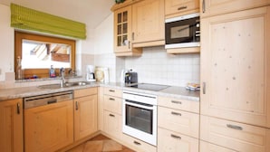 A kitchen with wooden cabinets, a built-in oven, a microwave, and a window with a green checkered blind. - Chalet in Hohe Tauern With Panoramic Views (Wald im Pinzgau)