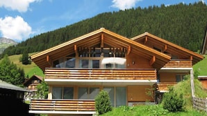 A wooden chalet with a balcony, large windows, and a mountainous backdrop. - Chalet in Hohe Tauern With Panoramic Views (Wald im Pinzgau)