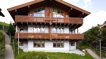 A two-story chalet with a wooden facade, multiple balconies, and a staircase leading up to the entrance.