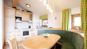 A compact kitchen with a dining area, featuring a wooden table, green upholstered seating, and white cabinets. - Chalet in Hohe Tauern With Panoramic Views (Wald im Pinzgau)