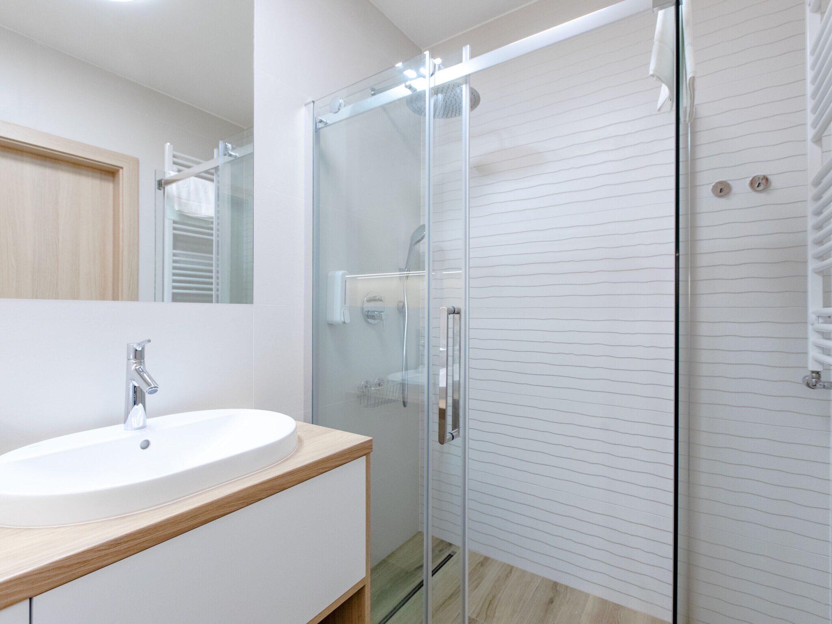 Un baño moderno con cabina de ducha de vidrio, lavabo blanco y tocador de madera.