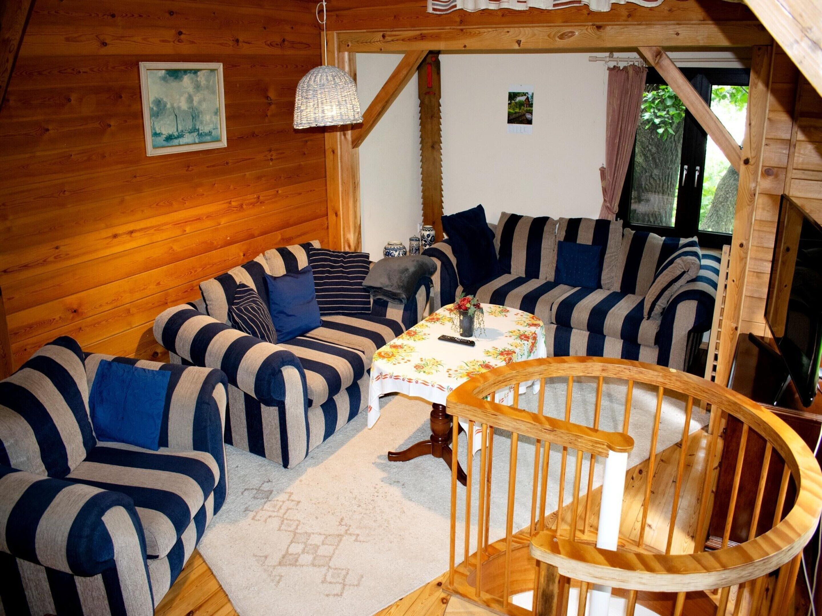 Een gezellig interieur van een chalet met gestreepte banken, een houten trap en een kleine tafel met een vaas.