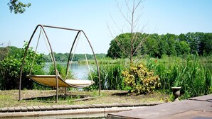 Una poltrona a dondolo vicino a uno stagno, con vista su una foresta e un cielo sereno.