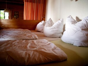A bedroom with a wooden headboard, a window with curtains, and multiple pillows on the bed. - Ferienhaus Seeblick in Goyatz (Schwielochsee)