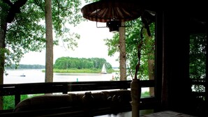 Vista dalla finestra su un lago con una barca a vela, alberi e una panchina con un vaso.