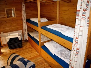 Una cabaña con tres literas, paredes de madera, una ventana pequeña y una cortina.