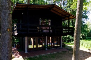 A wooden cabin with a balcony, surrounded by trees and a grassy area.