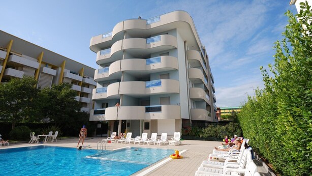 A modern multi-story building with a swimming pool and sun loungers. - Apartment in Bibione Near Beach and Pool (San Michele al Tagliamento)