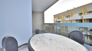 A balcony with a round marble table and four chairs, overlooking a building with yellow accents. - Apartment in Bibione Near Beach and Pool (San Michele al Tagliamento)