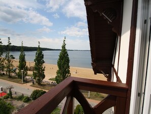 Une vue depuis un balcon donnant sur une plage, avec une balustrade en bois, un ciel dégagé et une mer calme.