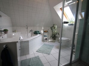 A modern bathroom with a bathtub, sink, and toilet. There is a potted plant and a shower area visible. - Ferienwohnung Am Strand in Schwerin (Schwerin)