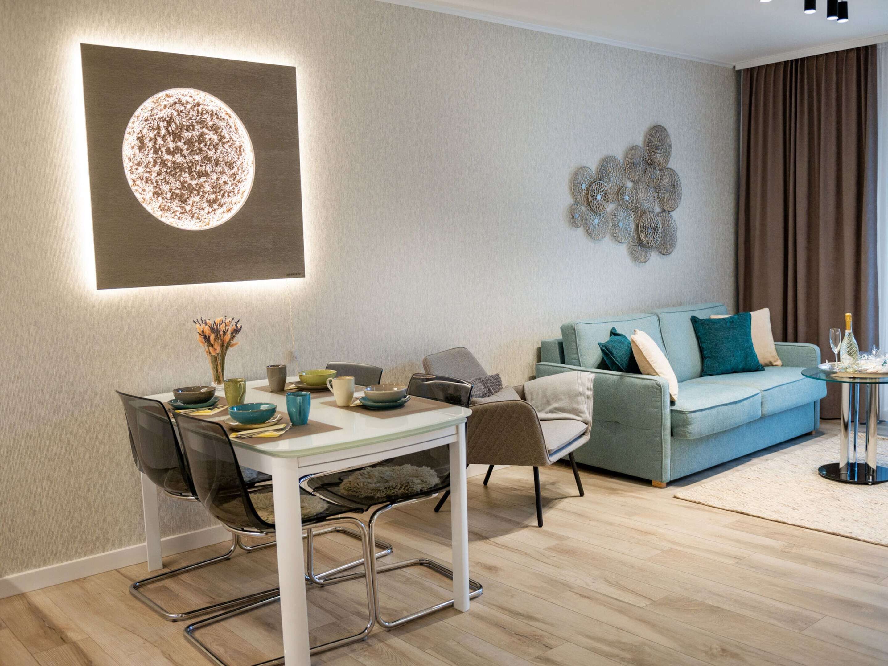 A modern living room with a dining area, featuring a round table, chairs, a sofa, and a decorative wall piece.