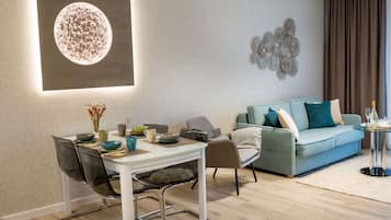A modern living room with a dining area, featuring a round table, chairs, a sofa, and a decorative wall piece.