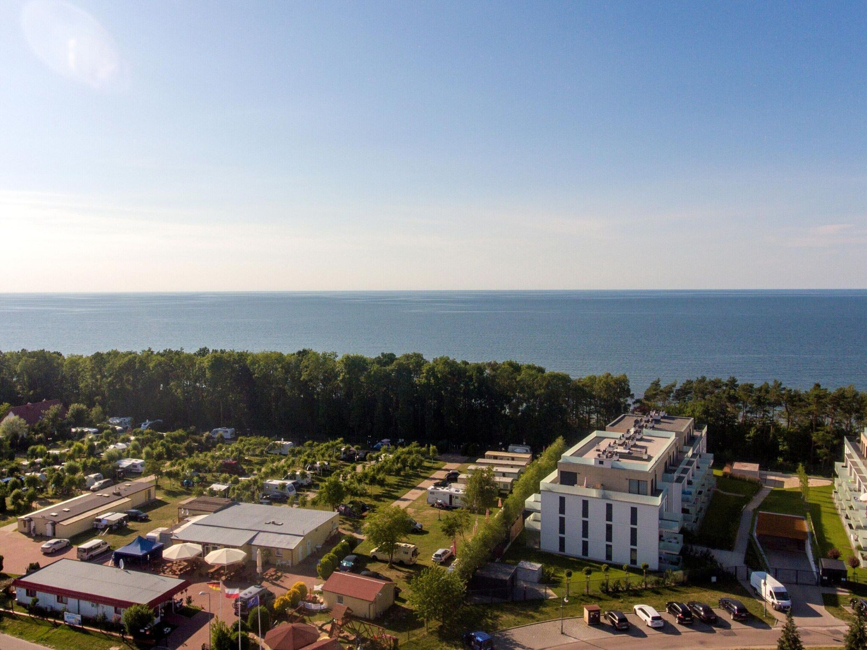 A coastal resort with a large building, multiple parking areas, and a view of the sea.