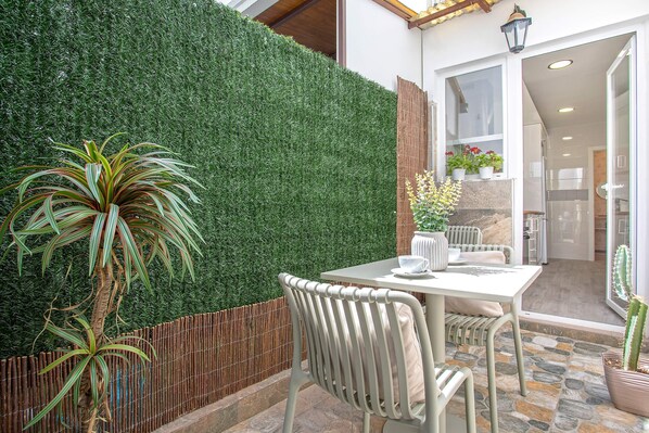 Un patio con una mesa, sillas, una planta en maceta y un seto verde.