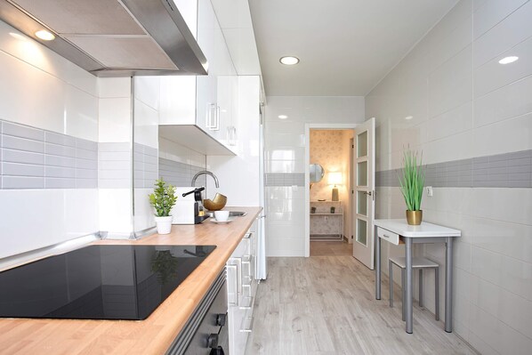 Una cocina moderna con armarios blancos, una placa de inducción negra y una encimera de madera.