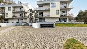 Ein modernes, mehrstöckiges Wohngebäude mit Balkonen, einem überdachten Außenbereich und einem gepflasterten Innenhof.