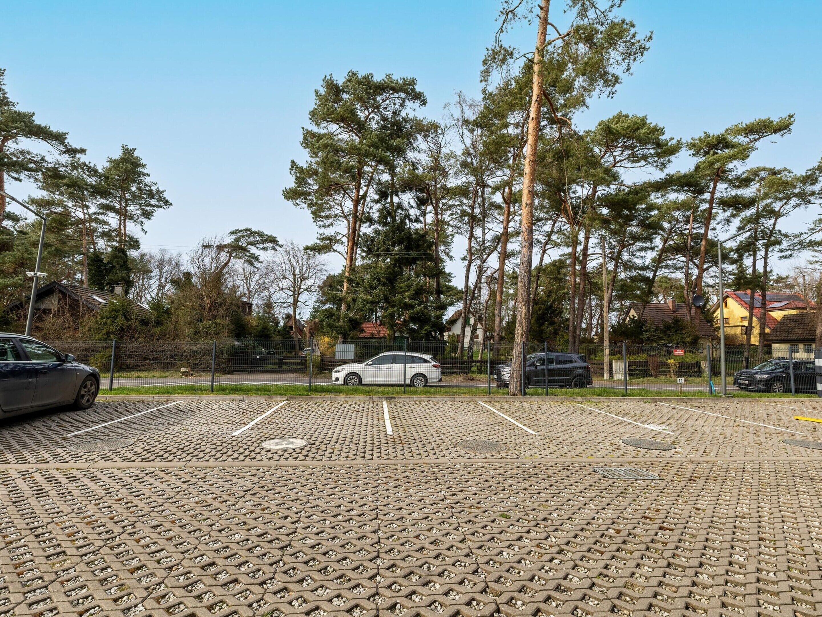 Un estacionamiento con pavimento estampado, rodeado de árboles y una valla.