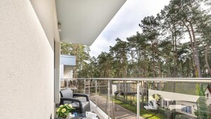 Ein Balkon mit Korbmöbeln, einem Blumentopf und Blick auf eine Wohngegend mit Bäumen und Häusern.