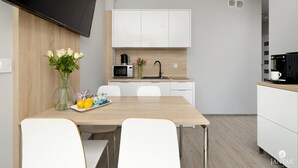 Eine moderne Küche mit weißen Schränken, einer Mikrowelle und einer Kaffeemaschine. Es gibt einen Esstisch mit Stühlen und eine Vase mit Blumen.