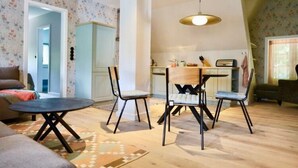 A living room with a sofa, a coffee table, and two chairs. There is a kitchen in the background with a dining table and chairs. - Reetgedecktes Ferienhaus in Nieblum auf Foehr (Nieblum)