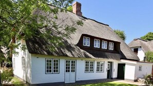 A traditional white cottage with a thatched roof, a small front porch, and a well-maintained lawn. - Reetgedecktes Ferienhaus in Nieblum auf Foehr (Nieblum)
