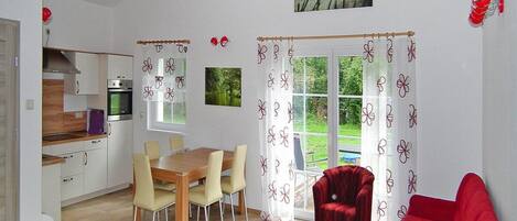 A spacious living area with a dining table, red sofa, and a kitchen in the background.