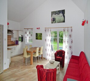 A spacious living area with a dining table, red sofa, and a kitchen in the background. - Ferienhaus Spreeidyll, Schlepzig (Schlepzig)