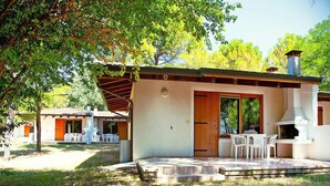 A rustic outdoor dining area with a stone patio, wooden pergola, and a grill station. - Bungalow in the Residence Belvedere in Grado (Aquileia)