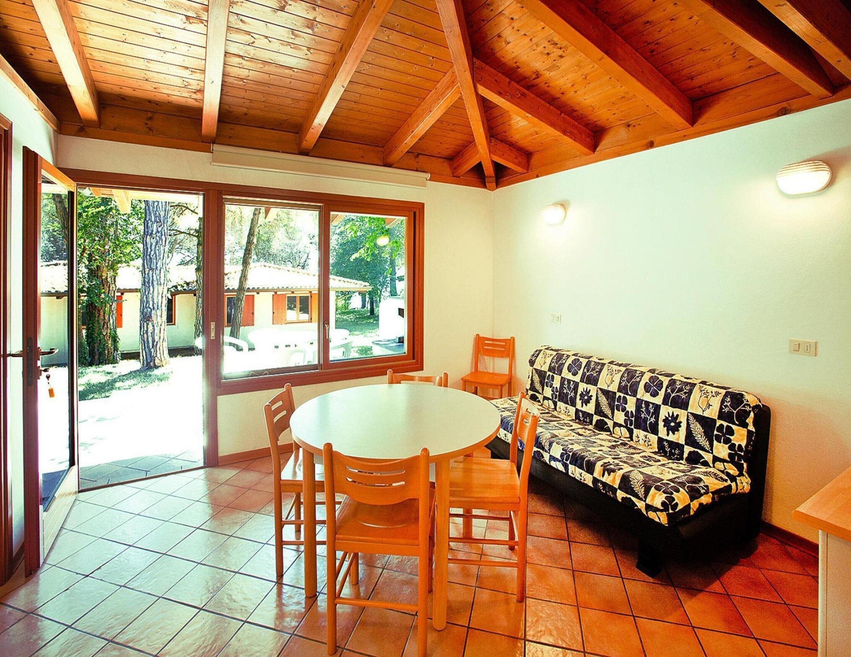 Una habitación con techo de madera, una mesa redonda con sillas para comer, un sofá estampado y un ventanal con vistas al exterior.