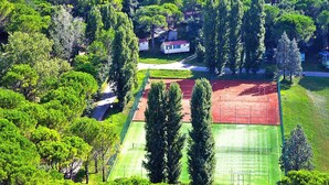 An aerial view of a residential area with a tennis court, surrounded by dense greenery and a few houses. - Bungalow in the Residence Belvedere in Grado (Aquileia)