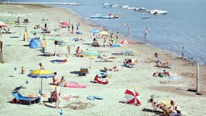 A beach with numerous umbrellas and sun loungers, a calm sea, and boats in the background. - Bungalow in the Residence Belvedere in Grado (Aquileia)