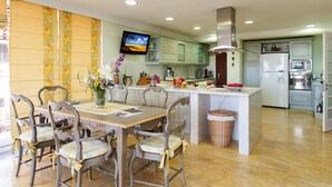 A modern kitchen with a central island, wooden chairs, a television, and a dining table. - Holiday Home, Maspalomas (San Bartolomé de Tirajana)