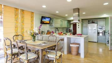 Uma cozinha moderna com ilha central, cadeiras de madeira, uma televisão e uma mesa de jantar.