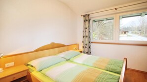 Una cama individual con cabecera de madera, una mesita de noche con lámpara y una ventana con cortinas.