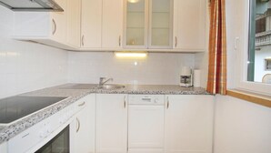 Cocina compacta con armarios blancos, horno empotrado, estufa y pileta.
