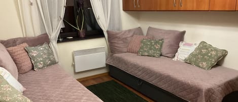 A bedroom with two beds, a radiator, a window with curtains, and a wooden wardrobe.